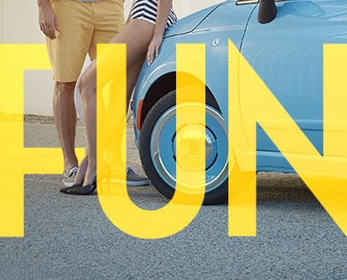 The word "Fun" in yellow over the driver-side front wheel area on a blue 2018 Fiat 500 with two people nearby.