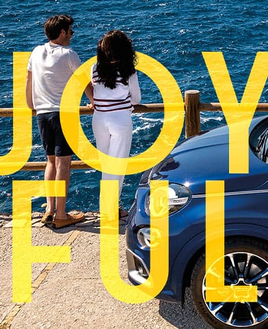 The word "Joyful" in yellow over a couple standing near the water's edge, with a blue 2022 Fiat 500X parked nearby.